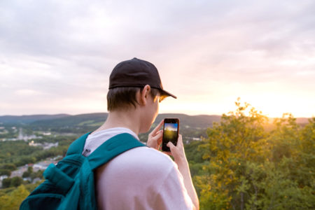Hartwick student using phone to take photo of sunrise at the top of Oyaron Hill