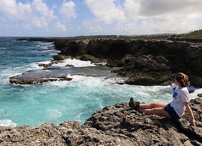 Hartwick student sitting on shoreline in Caribbean