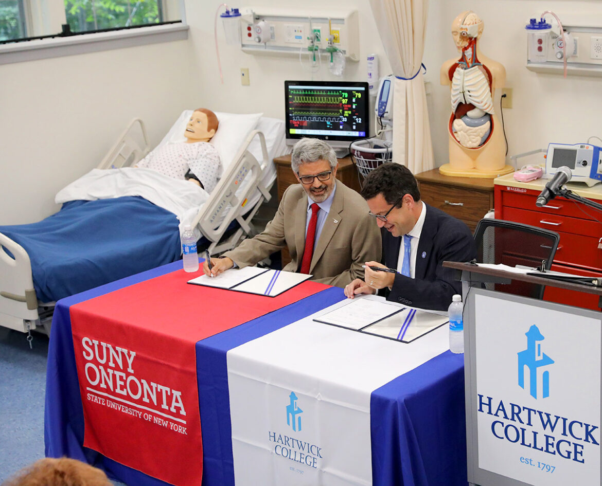 Hartwick College President Darren Reisberg and SUNY Oneonta President Alberto Cardelle put pen to paper, signing agreement.
