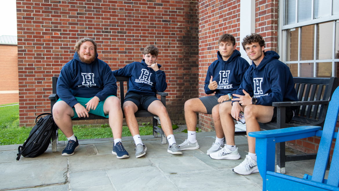 New Hartwick College students sitting on campus wearing new Hartwick sweatshirts during Wick Week