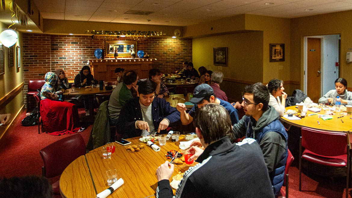 Hartwick students, faculty and staff attend the event Essence of Ramadan, students at tables eating and playing games.