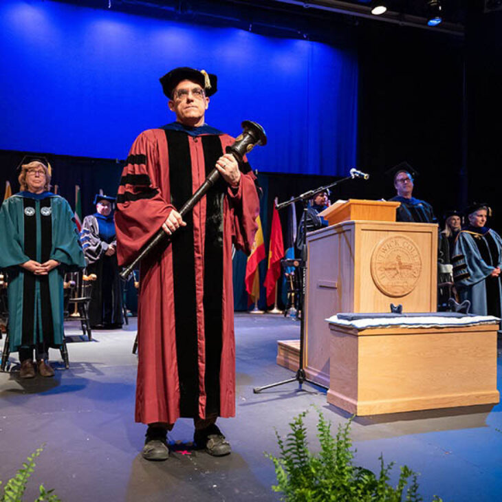 Faculty member on stage with platform party for Honors Convocation in Slade Theatre