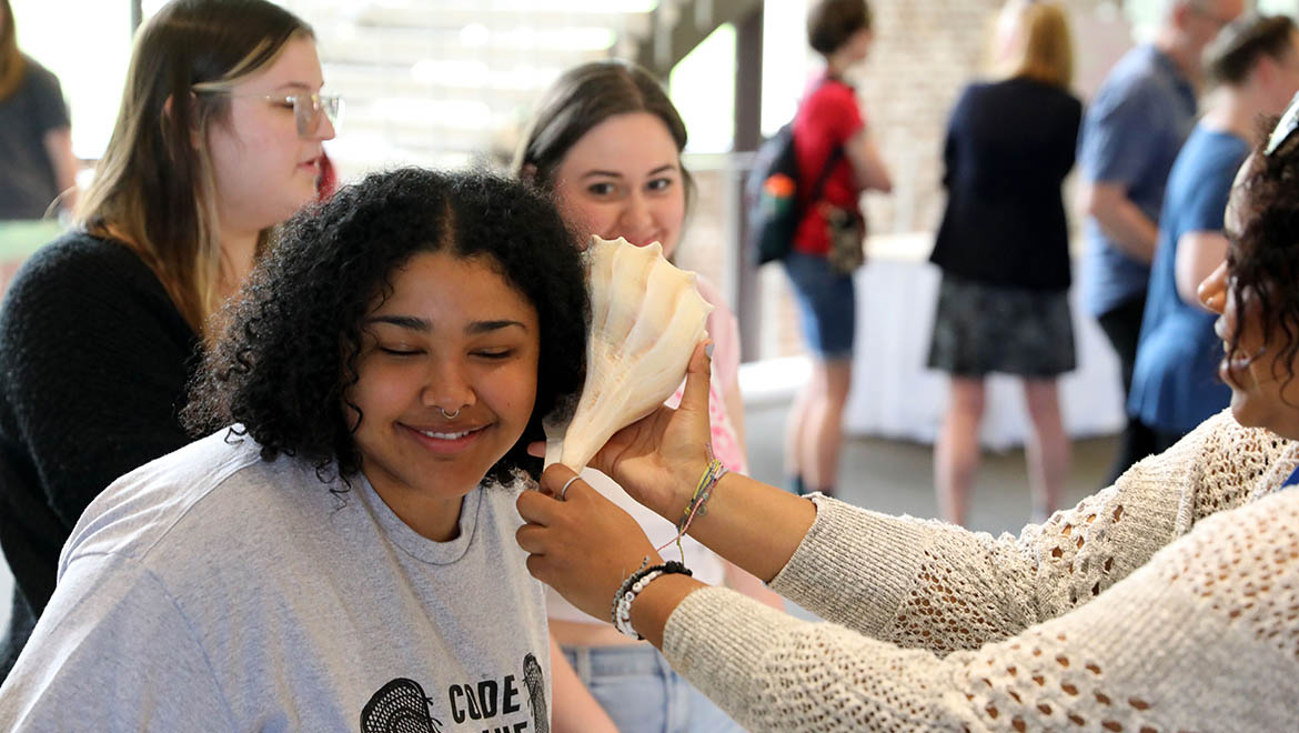 Hartwick student listening to sea shell during table top demonstration, Student Showcase