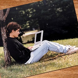 Hartwick College student sitting under tree using computer