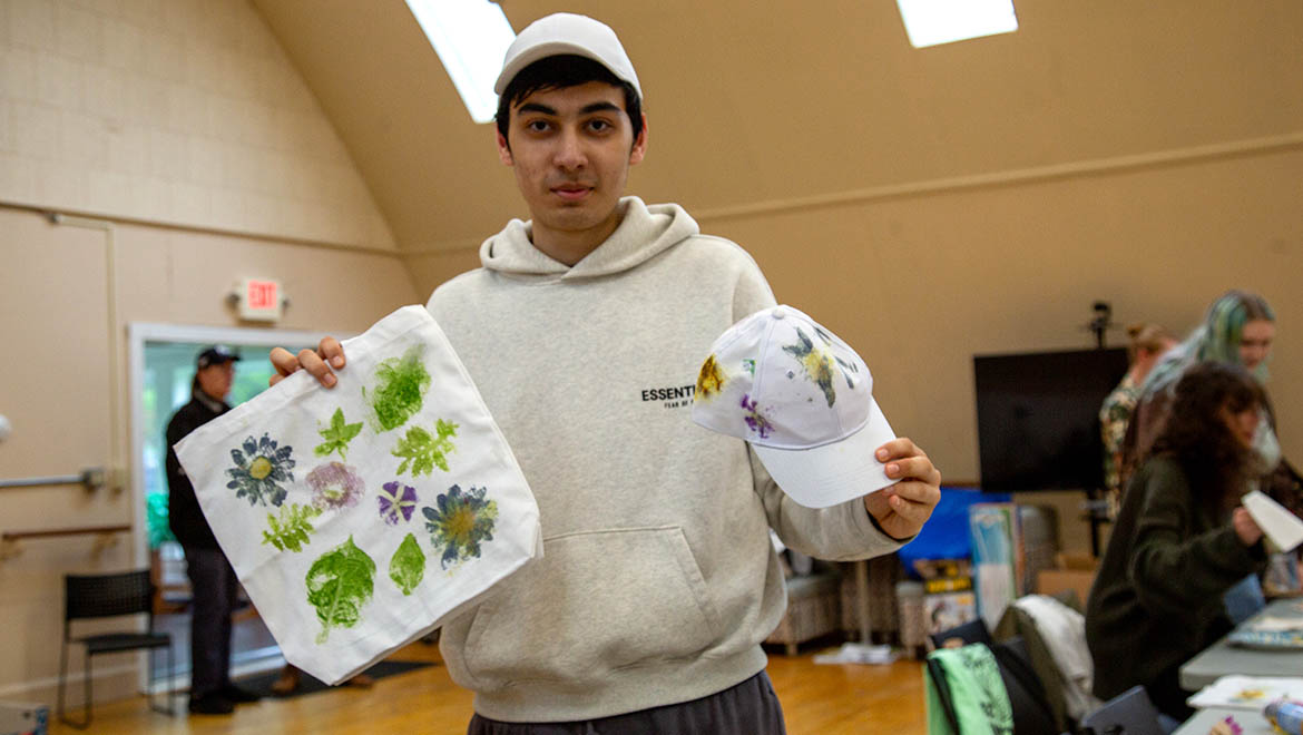 Hartwick College student holding nature prints he made during crafting event at Pine Lake