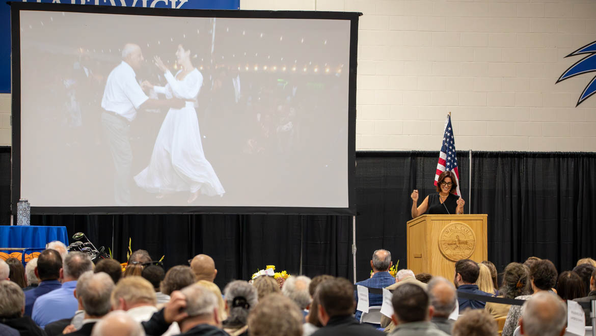 Jacey Lambros Carrino ’02 speaking about her father's dancing, shown in the slideshow while music played, during the Celebration of the Life of Nick Lambros in Lambros Arena