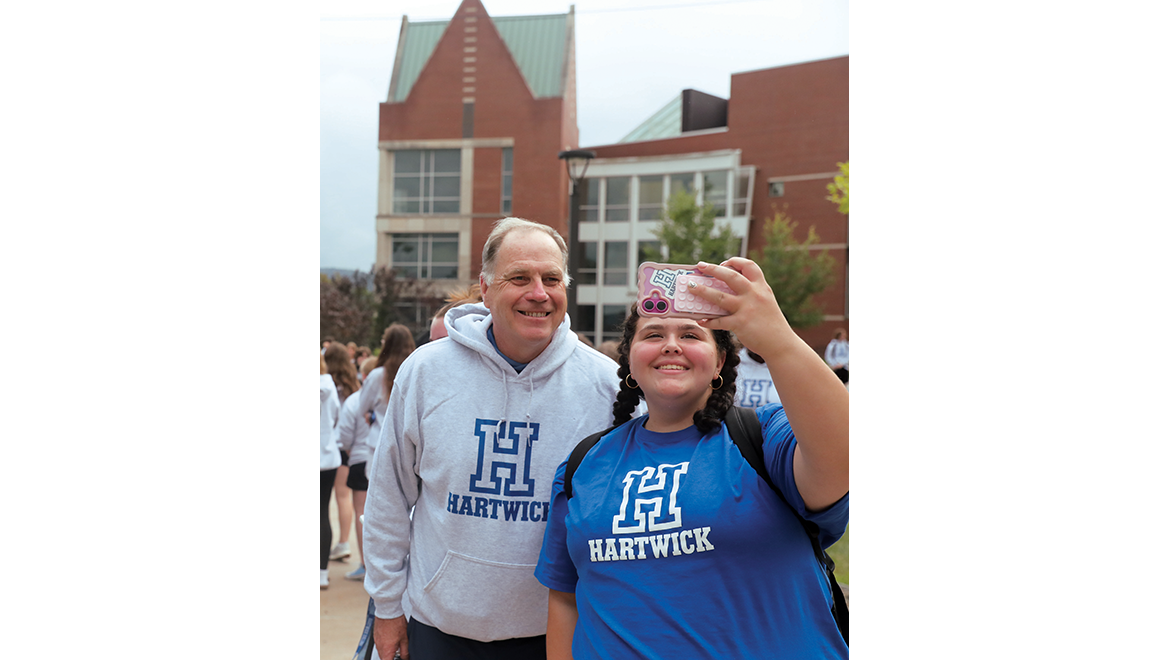 President Mullen with student taking a selfie on Founders' Way with Johnstone Science Center in the background