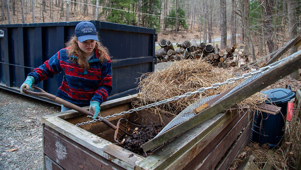 Abi DeMan ’26 turning over material in the compost bin at Pine Lake