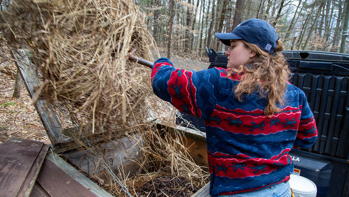 Abi DeMan ’26 addin hay to compost bin at Pine Lake
