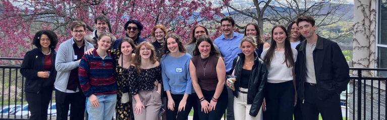 Hartwick College STEM students outside of Johnstone Science Center with spring tree in bloom and mountain view