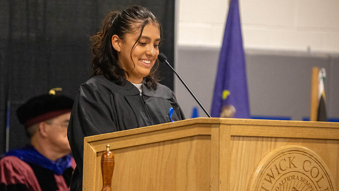 Hartwick College Student Government Association President Rebeka Alva ’27 speaking into a microphone at a wooden podium during Opening Convocation.