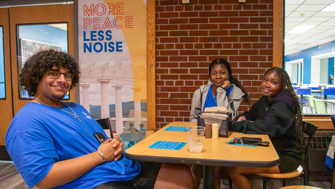 Three Hartwick College students sit at a table in a cafeteria, smiling.