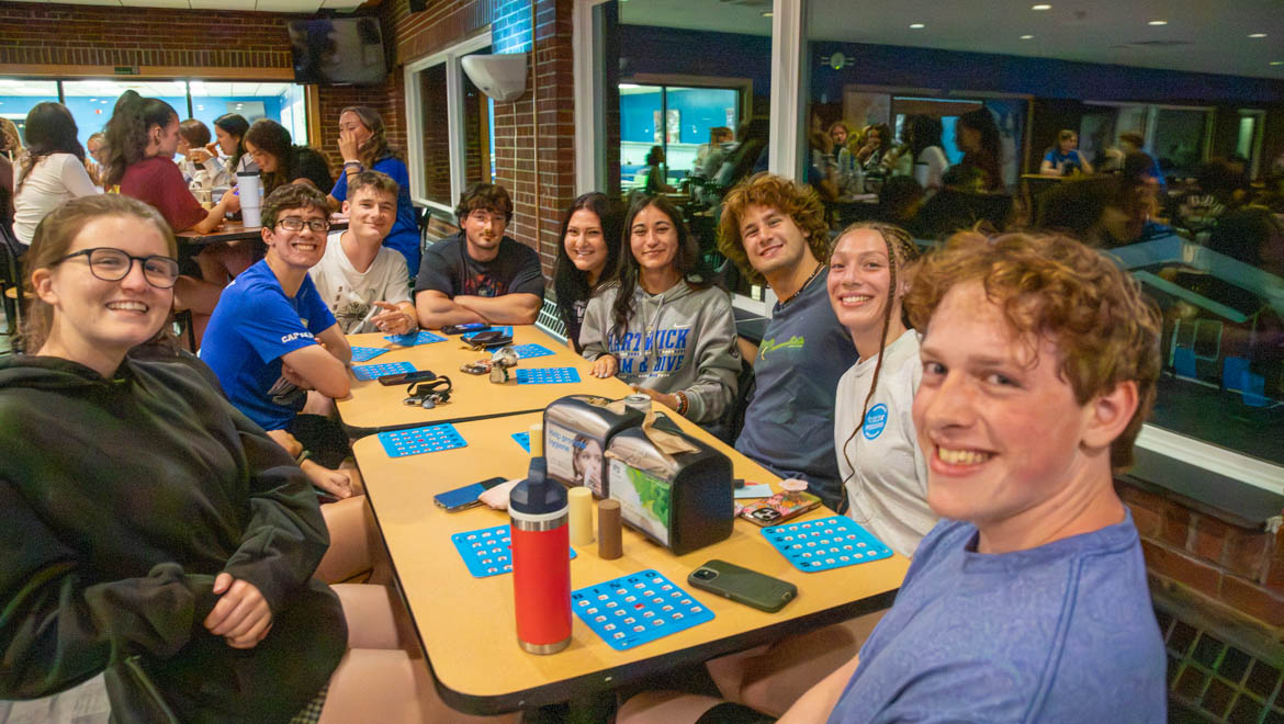A group of smiling Hartwick students sitting around tables playing bingo during Wick Weekend for new students