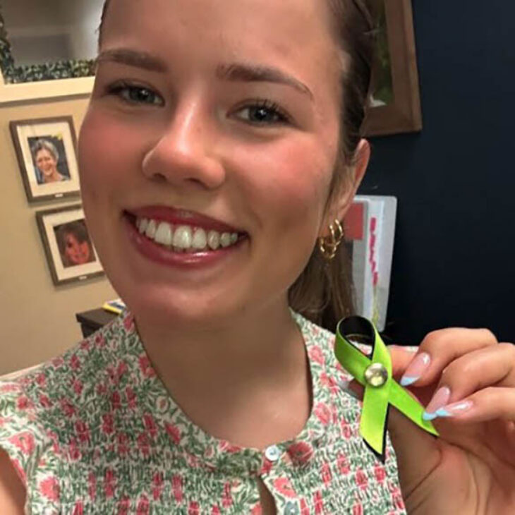 Portrait of Savannah Evans holding up a lime green awareness ribbon with a silver button.
