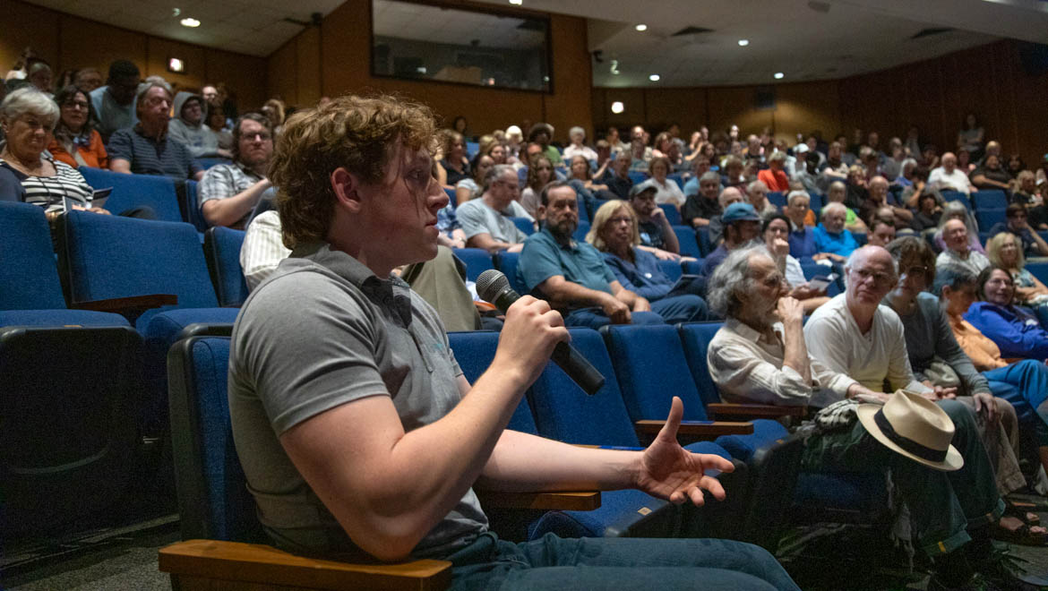 An audience watches as member of audience asks a question of Mike McIntire on a stage in an auditorium.