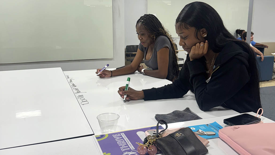 THRIVE students writing on a white dry-erase table with markers in a classroom setting.