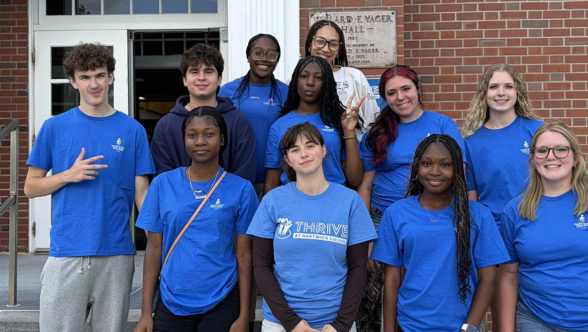 Hartwick College THRIVE students in blue t-shirts smiling in front of a brick building with a sign for Willard E. Yager Hall.