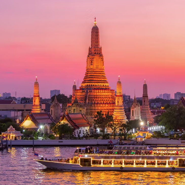 Wat Arun temple in Bangkok, lit up at dusk with a pink and orange sky, and an illuminated tour boat on the river.