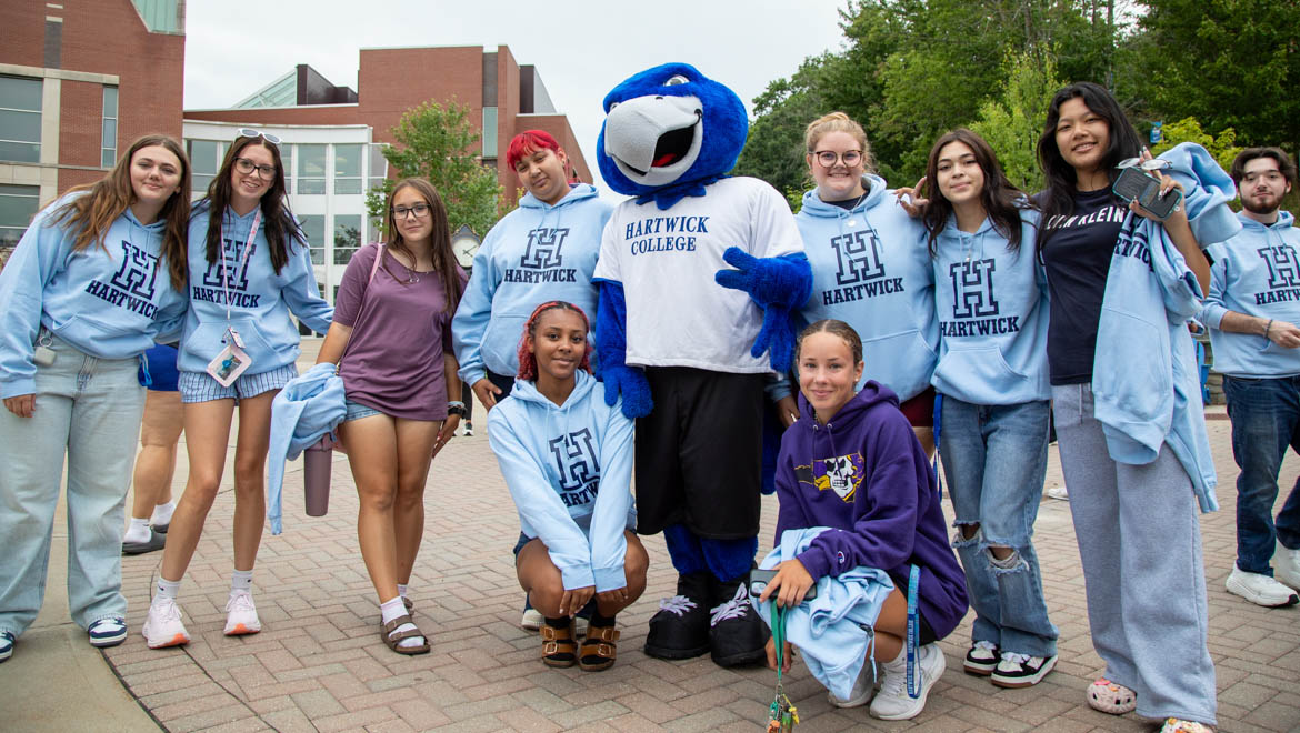 Hartwick new students with Swoop the Hartwick College mascot pose outdoors on campus, many wearing light blue Hartwick hoodies during First Walk