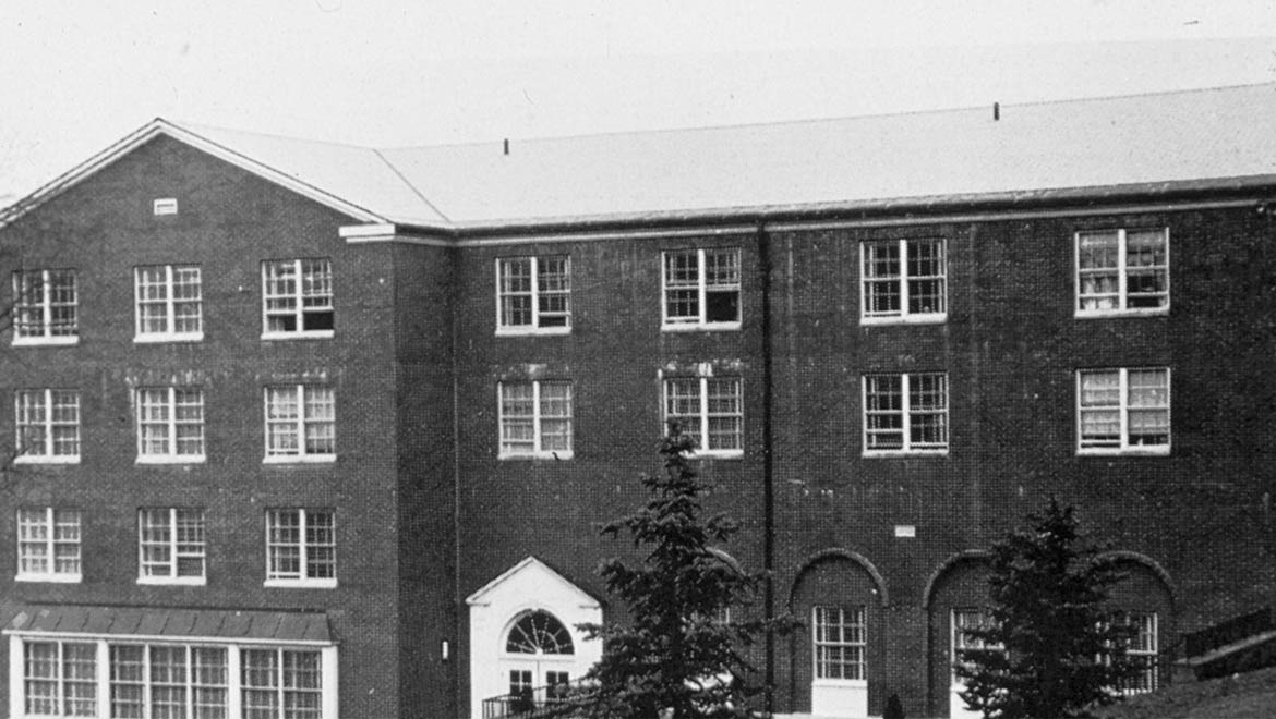 Black and white photo of Hartwick College's Saxton Hall with many multi-paned windows, a gabled roof section, and arched entrances.